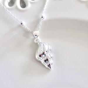 May include: A silver necklace with a delicate chain and a small, detailed seashell pendant.