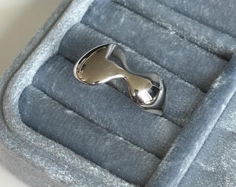 May include: A silver ring with a unique, abstract design. The ring is smooth and shiny, and it has a modern, minimalist aesthetic.