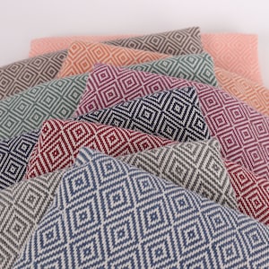 May include: A stack of ten patterned throw pillows in various colours, including navy blue, grey, red, pink, and green. The pillows feature a diamond pattern.