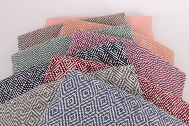 May include: A stack of ten patterned throw pillows in various colours, including navy blue, grey, red, pink, and green. The pillows feature a diamond pattern.