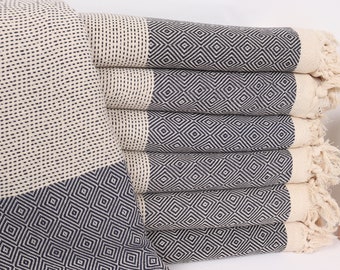 May include: A stack of six white and navy blue Turkish towels with fringe edges. The towels feature a geometric diamond pattern.