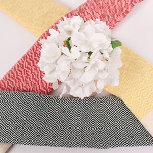 May include: Three Turkish towels with a diamond pattern in yellow, red and black. The towels are arranged in a cross shape with a bouquet of white flowers in the centre.