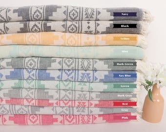May include: A stack of 12 patterned towels in various colors, including navy, black, yellow, mint, dark green, sax blue, green, dark gray, red, gray, and pink. The towels are folded and stacked on a white surface. Each towel has a different color and a geometric pattern.