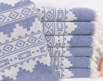 May include: A stack of blue and white patterned Turkish towels with fringe. The towels have a geometric design and are folded neatly.