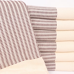May include: A stack of white Turkish towels with a brown geometric pattern. The towels have fringe on the ends.