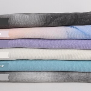 May include: Six different colored blankets stacked on top of each other. The colors are black, rainbow, purple, natural, petrol blue, and gray.