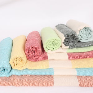 May include: A stack of colourful Turkish towels with fringe, folded and rolled, in shades of orange, yellow, blue, green, and red.