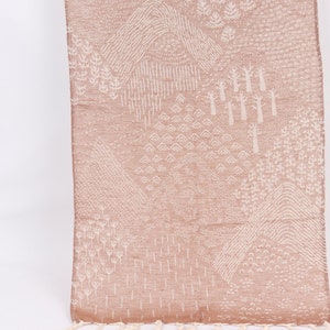 Könnte beinhalten: Ein gewebter Teppich in Blush-Farbe mit einem weißen geometrischen Muster aus Bäumen, Bergen und anderen naturinspirierten Designs.