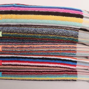 May include: A stack of colorful striped beach towels. The towels are labeled "Multicolor 1" through "Multicolor 5". The towels have a variety of colors including blue, red, pink, yellow, and brown. The towels have fringed edges.