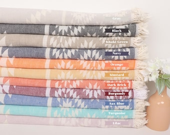 May include: A stack of 11 Turkish towels in various colors, including gray, black, khaki green, navy, orange, mustard, dark brick, burgundy, sax blue, turquoise, and lilac. Each towel features a geometric pattern.