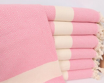 Può includere: Un mucchio di asciugamani turchi rosa e bianchi con un motivo a rombi. Gli asciugamani hanno frange alle estremità.
