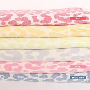 Pode incluir: Uma pilha de seis toalhas coloridas com padrões e bordas franjadas. As toalhas são empilhadas em um padrão de arco-íris, começando com vermelho, amarelo, verde claro, cinza claro, rosa e azul escuro. Cada toalha tem um padrão de leopardo.