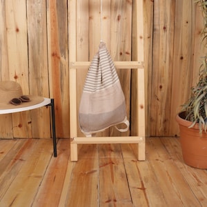 May include: A drawstring backpack featuring a woven pattern with horizontal stripes in shades of beige, cream, and dark brown. The bag has a tapered shape with a gathered top closure and two thin straps attached at the bottom corners for carrying.