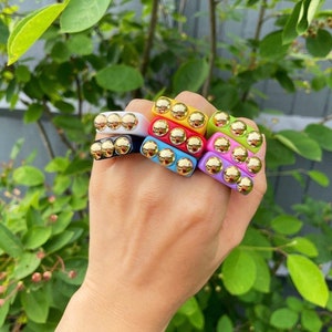 May include: A stack of colorful square rings with gold accents. The rings are made of plastic and have a smooth, glossy finish.