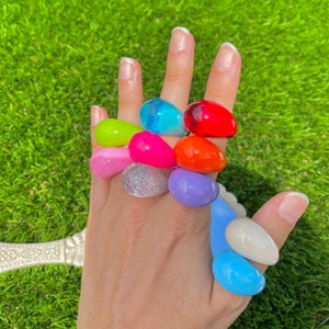 May include: A set of colourful, oval-shaped rings made of plastic. The rings are in various colours, including pink, blue, green, red, and orange. The rings are stacked on a person's fingers.