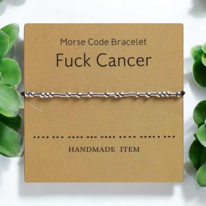 Puede incluir: Una tarjeta marrón con el texto "Morse Code Bracelet" y "Fuck Cancer" en letras negras. Un brazalete de cuentas plateadas se muestra en la tarjeta. El brazalete está hecho de pequeñas cuentas plateadas conectadas por finas barras plateadas. La tarjeta también incluye el texto "HANDMADE ITEM" y una fila de puntos y guiones que representan el código Morse de la frase "Fuck Cancer".