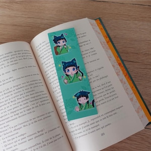 Op de afbeelding: Een turquoise bladwijzer met drie illustraties van een cartoonfiguur met zwarte kattenoren. Het personage draagt een groene en witte outfit en heeft zwart haar. De bladwijzer heeft een witte achtergrond met groene en roze accenten.