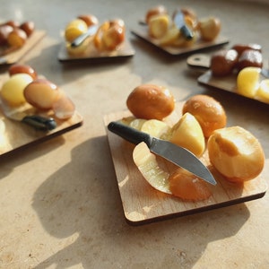 Könnte beinhalten: Fünf Miniatur-Schneidebretter aus Holz mit Miniaturmessern und Kartoffeln. Die Kartoffeln sind ganz, geschnitten und geschält.