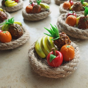 Könnte beinhalten: Ein kleiner, geflochtener Korb gefüllt mit Miniaturfrüchten, darunter eine Ananas, Bananen, Orangen und ein Apfel. Die Früchte sind aus Polymer Clay gefertigt und realistisch angeordnet.