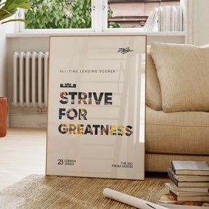 May include: A motivational poster with a gold frame featuring LeBron James and the text "STRIVE FOR GREATNESS". The poster is hanging on a white wall in a living room with a large window, a potted plant, a wooden chair, and a couch.