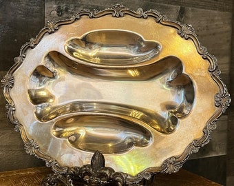 Pode incluir: Um prato de servir de prata com três seções. O prato tem uma borda decorativa e ornamentada e está sentado em um suporte de metal preto.