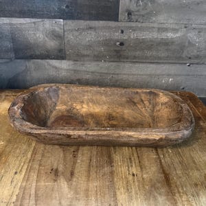May include: A rustic wooden serving bowl with a natural brown finish. The bowl is oval shaped and has a slightly raised rim.