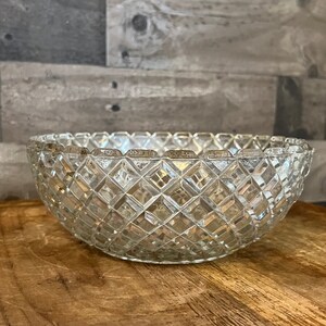May include: A clear glass bowl with a diamond pattern. The bowl is empty and sitting on a wooden surface.