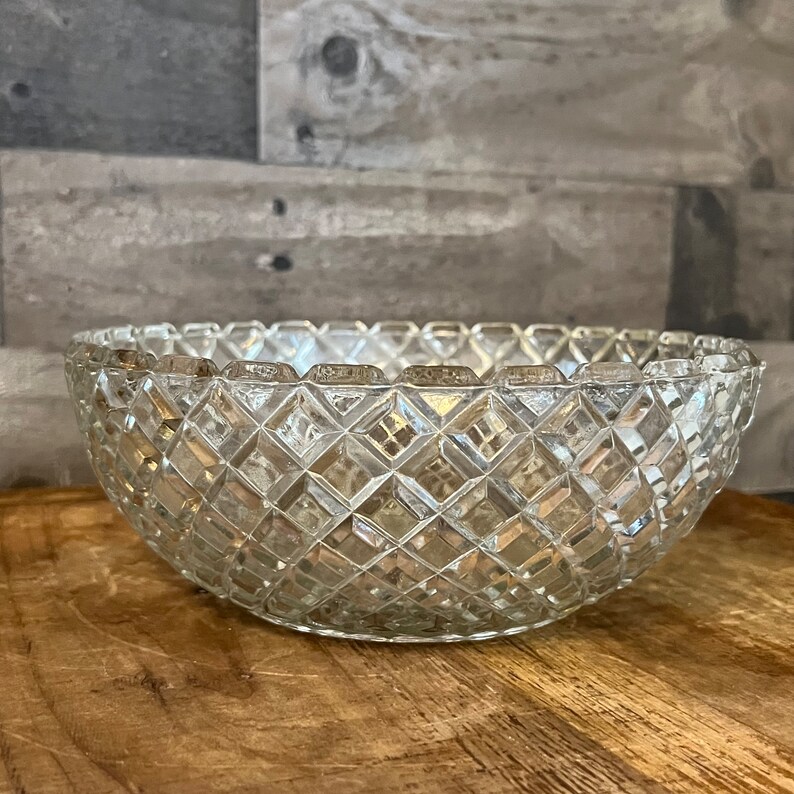 May include: A clear glass bowl with a diamond pattern. The bowl is empty and sitting on a wooden surface.