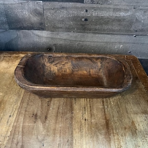 May include: A rustic wooden dough bowl with a natural brown finish. The bowl is oval shaped and has a slightly raised rim.