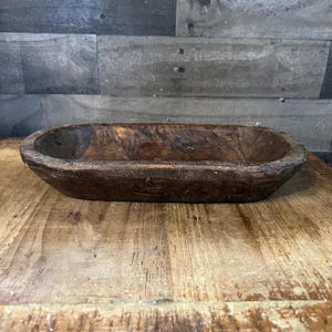 May include: A rustic wooden dough bowl with a natural brown finish. The bowl is oval shaped and has a slightly raised rim.