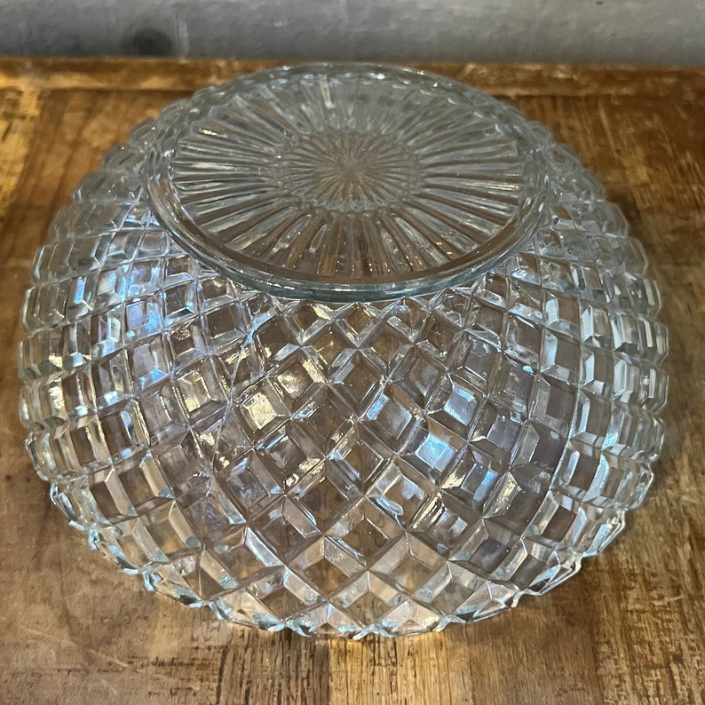 May include: A clear glass bowl with a diamond pattern. The bowl is empty and has a smooth, shiny surface.
