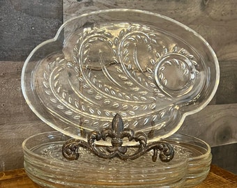 May include: A set of clear glass serving dishes with a decorative leaf pattern. The dishes are stacked on a metal stand with a fleur-de-lis design.