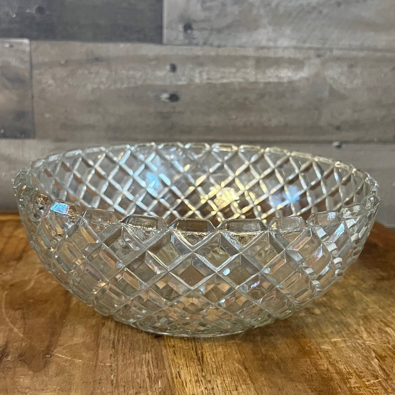May include: A clear glass bowl with a diamond pattern. The bowl is empty and sitting on a wooden surface.