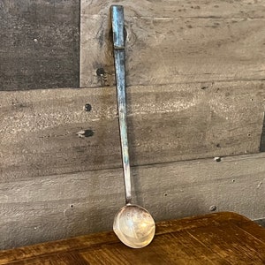 May include: A long, silver ladle with a rounded bowl. The handle is straight and has a decorative band near the top.