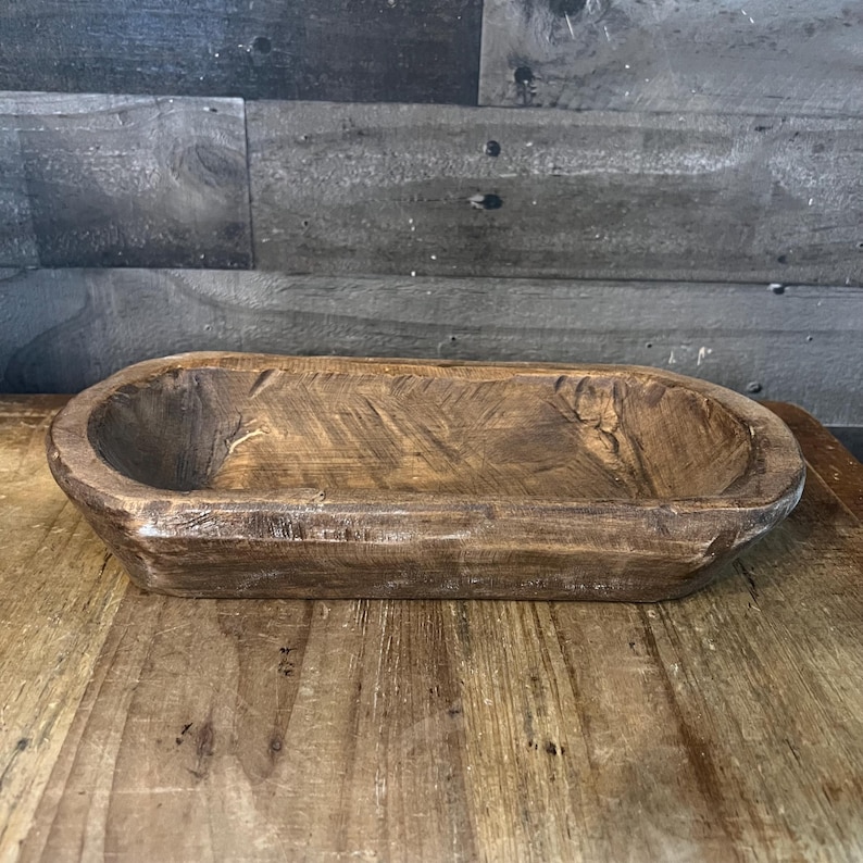 May include: A rustic wooden serving bowl with a natural brown finish. The bowl is oval shaped and has a slightly raised rim.