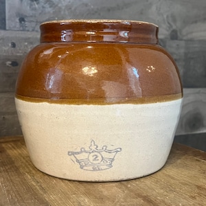 Puede incluir: Una olla de barro esmaltada en marrón y blanco con una corona azul y el número "2" en la parte inferior.