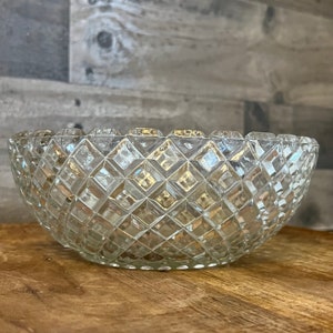 May include: A clear glass bowl with a diamond pattern. The bowl is empty and sitting on a wooden surface.
