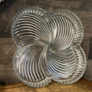 Peut inclure: Un plat de service en verre transparent avec un motif en spirale. Le plat comporte quatre sections et est parfait pour servir des en-cas ou des amuse-gueules.