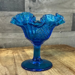 Op de afbeelding: Een blauwe glazen snoepkom met een gekrulde rand en een diamantpatroon. De kom heeft een voet.