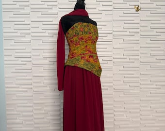 May include: A floor-length maroon dress featuring a strapless bodice with a textured yellow and green patterned overlay. The garment includes a matching maroon shawl draped over one shoulder and a long, flowing skirt made of a sheer, lightweight fabric.