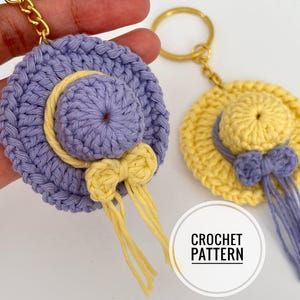 May include: Two crochet hat keyrings. One is lavender with a yellow bow and trim, the other is yellow with a lavender bow and trim. Both have gold key rings. The image includes the text "CROCHET PATTERN".