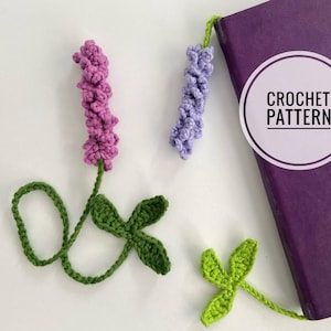 Puede incluir: Dos marcapáginas de lavanda hechos a crochet con hojas verdes. Los marcapáginas están unidos a un libro morado con el texto "CROCHET PATTERN" en la portada.