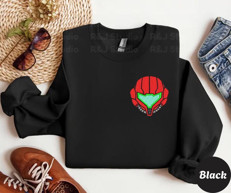 Black color unisex crewneck sweatshirt featuring a retro sumas bounty hunter helmet embroidery with red armor panels and neon green visor, minimalist gamer streetwear style
Close up sleeve detail showing embroidered retro sumas helmet patch with red stitching and bright green visor on neutral sand crewneck sweatshirt