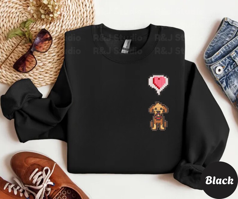 Black unisex crewneck sweatshirt showcasing a pixel art embroidered Stardew Valley dog with a red heart icon. The contrast stitching enhances the classic farming game aesthetic, making it a cozy gamer apparel choice for Stardew Valley fans, relaxed streetwear looks, indie game inspired outfits, and thoughtful gaming gifts.