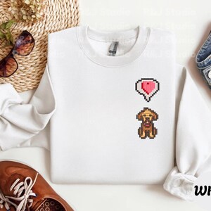 White unisex sweatshirt with a clean embroidered Stardew Valley dog design in retro pixel art style, accented with a small red heart symbol. The minimalist look emphasizes the cozy farming game vibe, perfect for Stardew Valley enthusiasts, casual gamer outfits, indie game merchandise collectors, and everyday cozy wear.
