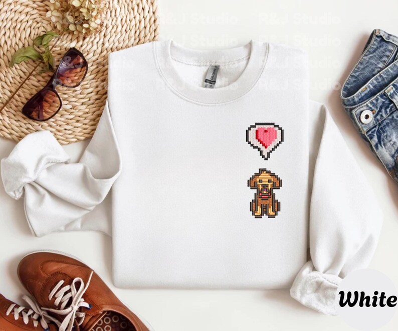 White unisex sweatshirt with a clean embroidered Stardew Valley dog design in retro pixel art style, accented with a small red heart symbol. The minimalist look emphasizes the cozy farming game vibe, perfect for Stardew Valley enthusiasts, casual gamer outfits, indie game merchandise collectors, and everyday cozy wear.
