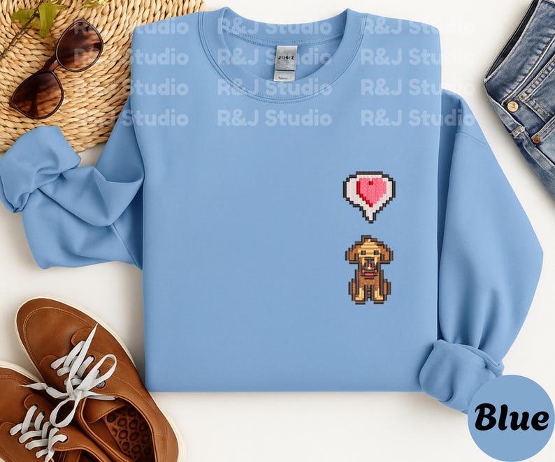 Light blue unisex crewneck sweatshirt featuring a small embroidered Stardew Valley pixel dog with a red heart icon. The design reflects the calming, cozy farming game atmosphere of Stardew Valley, making it suitable for everyday casual wear, indie game lovers, pixel art fans, and comfortable gamer themed clothing.