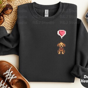 Dark Heather unisex crewneck sweatshirt showcasing a pixel art embroidered Stardew Valley dog with a red heart icon. The contrast stitching enhances the classic farming game aesthetic, making it a cozy gamer apparel choice for Stardew Valley fans, relaxed streetwear looks, indie game inspired outfits, and thoughtful gaming gifts.