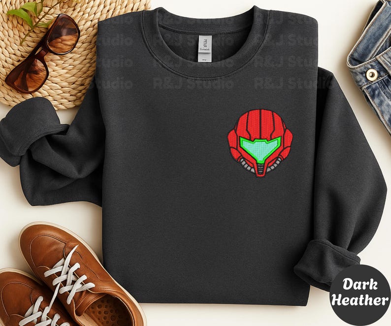 Dark Heather color unisex crewneck sweatshirt featuring a retro sumas bounty hunter helmet embroidery with red armor panels and neon green visor, minimalist gamer streetwear style
Close up sleeve detail showing embroidered retro sumas helmet patch with red stitching and bright green visor on neutral sand crewneck sweatshirt