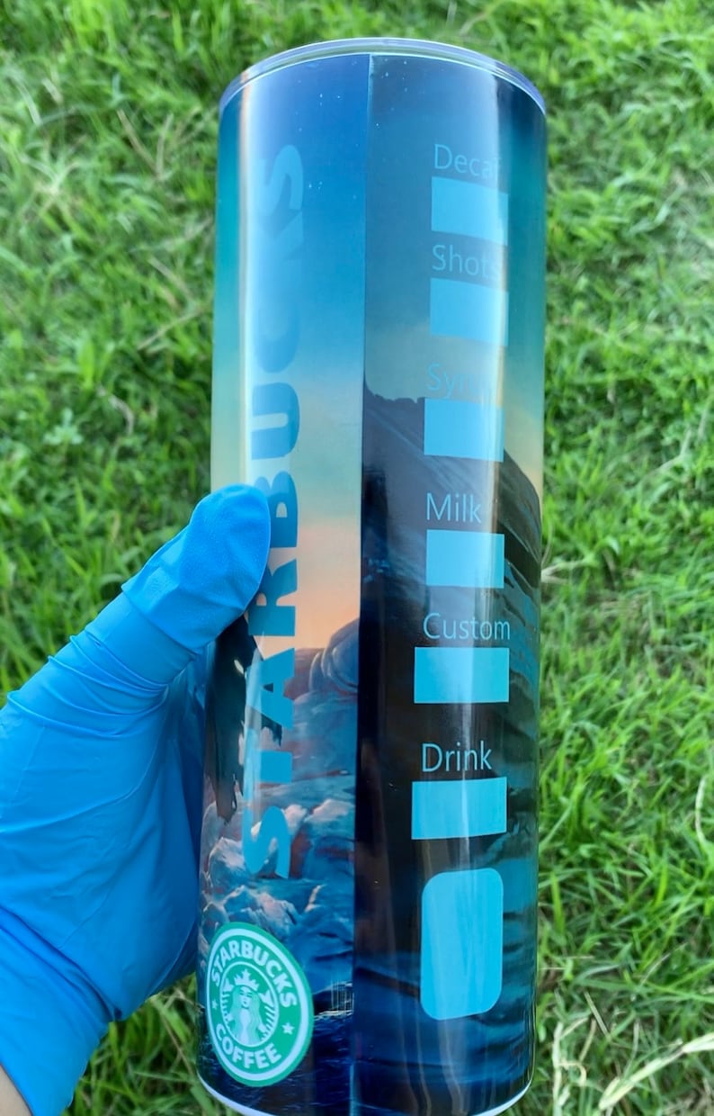 May include: A blue and white stainless steel tumbler with a Starbucks logo and a mountain scene. The tumbler has a list of drink options on the side, including decaf, shots, syrup, milk, custom, and drink.